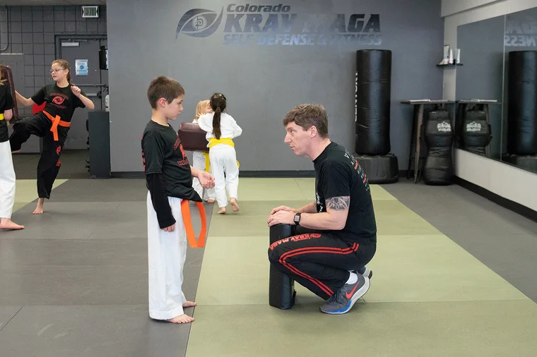 A Colorado Krav Maga instructor kneeling to coach a young student