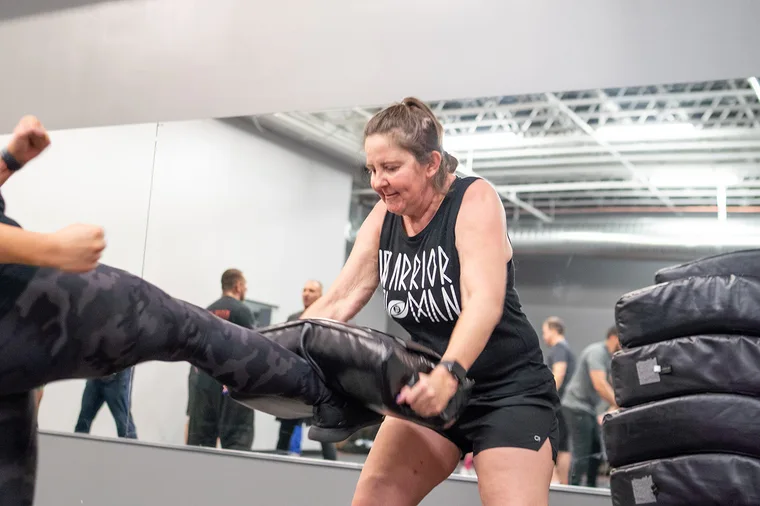 An adult student landing a powerful kick on a pad in a Colorado Krav Maga class