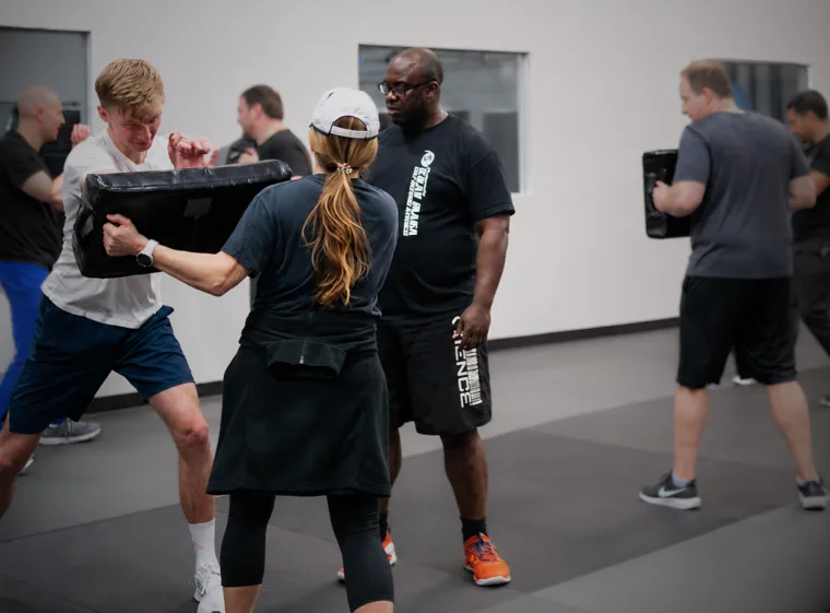 A Colorado Krav Maga instructor coaching an adult student on pad work